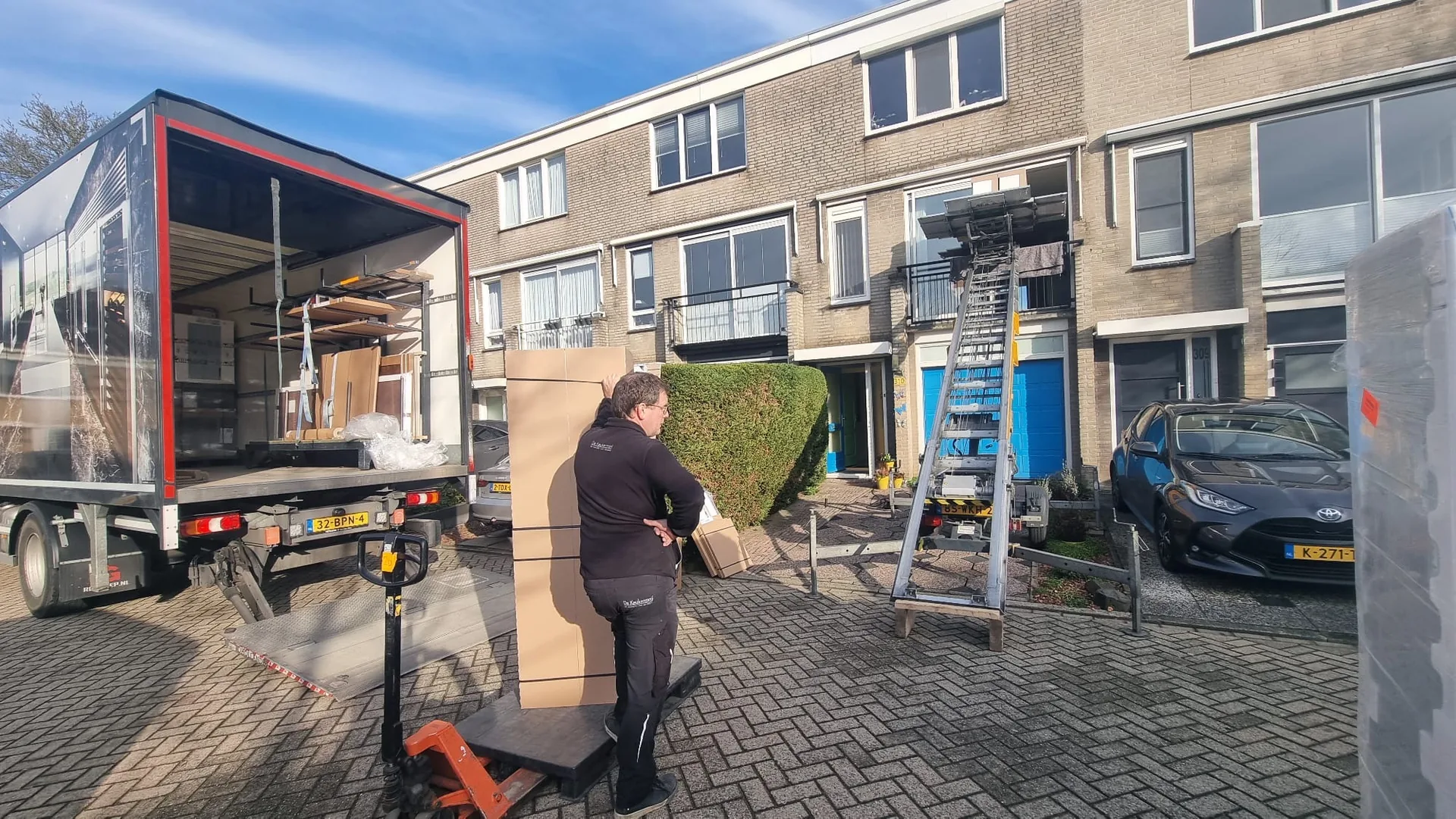 Verhuizer laadt dozen bij de verhuiswagen, ladderlift op de achtergrond